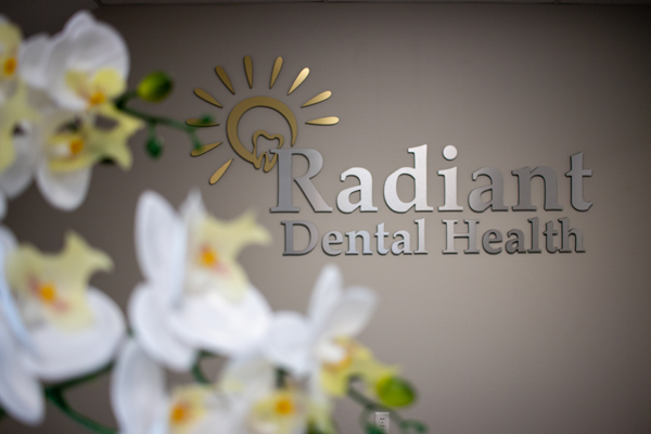 Radiant Dental Health logo on a wall behind flowers at their front desk.